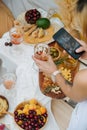 Woman taking picture of wine glass in hand over a table with various appetizers