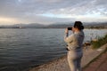 Woman taking pictures on a smartphone of a cloudy sunset on the sea Royalty Free Stock Photo