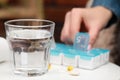 Woman taking pill from plastic box at white table indoors, focus on glass of water. Space for text Royalty Free Stock Photo