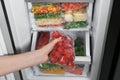 Woman taking plastic bag with frozen tomatoes from refrigerator