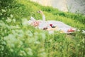 A woman is taking a selfie lying on the grass on a blanket. Lady on picnic looking at phone