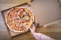 Woman taking slice of delicious pizza from cardboard box. Top view on brown wooden table Royalty Free Stock Photo