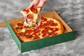 Female hand taking slice of pizza with melted cheese, pepperoni and jalapeno from cardboard box Royalty Free Stock Photo