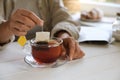 Woman taking tea bag out of cup at white wooden table indoors, closeup. Space for text Royalty Free Stock Photo