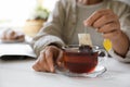 Woman taking tea bag out of cup at white wooden table indoors, closeup. Space for text Royalty Free Stock Photo