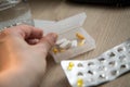 Woman taking yellow pills tablets medicine of blister and pillbox with glass of water on wooden nightstand table Royalty Free Stock Photo