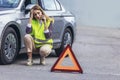 Woman, talking on her cell phone while her car is broken down on the road with reflective warning triangles Royalty Free Stock Photo