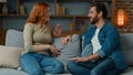 Woman talking with man at home joyful Caucasian couple sit on couch redhead girl telling funny story positive diverse Royalty Free Stock Photo