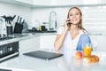 Young woman talking on mobile phone while using laptop in kitchen at home Royalty Free Stock Photo