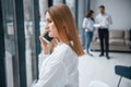 Woman talking by phone in front of group of young successful team that working and communicating together indoors in Royalty Free Stock Photo