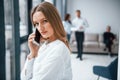 Woman talking by phone in front of group of young successful team that working and communicating together indoors in Royalty Free Stock Photo