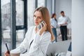 Woman talking by phone in front of group of young successful team that working and communicating together indoors in Royalty Free Stock Photo