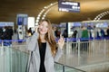 Woman talking by smartphone at airport hall, wearing grey coat and black bag, showing ok. Royalty Free Stock Photo