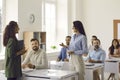 Woman talking to business coach while other students are sitting at desks and listening Royalty Free Stock Photo