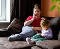 Woman is talking to a cell phone and girl playing on tablet. Mom and daughter stay at home, sitting on a sofa in living room Royalty Free Stock Photo