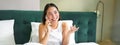 Woman talks on mobile phone in bed. Smiling girl having telephone conversation while relaxing in bedroom Royalty Free Stock Photo