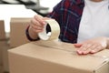 Woman taping cardboard box indoors, closeup. Moving day