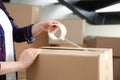 Woman taping cardboard box indoors, closeup. Moving day