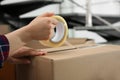 Woman taping cardboard box indoors, closeup view