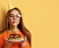 Woman with tasty big beef burger barbeque sandwich for birthday party with lit candle on pastel yellow Royalty Free Stock Photo