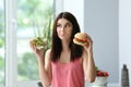 Woman with tasty burger and fresh salad indoors. Choice between healthy and unhealthy food