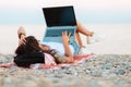 A woman with a tattoo on her arm lies on the beach on the sand and works on a laptop. Rear view. The concept of remote work and