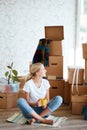 Woman with tea in hand sitting on floor of new apartment, pile of moving boxes on background Royalty Free Stock Photo