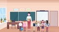 Woman teacher with mix race pupils standing in modern school classroom interior chalk board desk cartoon characters full