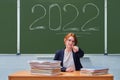 Woman teacher in school class with chalk inscription 2022 on blackboard. Coronavirus problem in the new school year, copy space