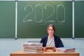 Woman teacher sits at table on blackboard background with text 2020. Concept of learning problems during the global crisis due to Royalty Free Stock Photo