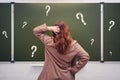 Woman teacher stands pensively against the background of a school blackboard with question marks Royalty Free Stock Photo