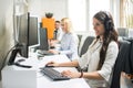 Woman telephone operator with headset working on computer in row in customer call support helpline center with coworkers Royalty Free Stock Photo