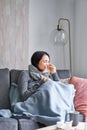 Woman with temperature, coughing, showing symptoms of flu, influenza or cold, sitting in warm clothes on sofa, covered Royalty Free Stock Photo