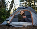 Woman in a tent drinking tea on vacation. Forest background. Camping and tourism.Rest in nature