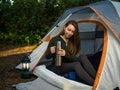 Woman in a tent drinking tea on vacation. Forest background. Camping and tourism.Rest in nature