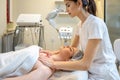 Woman, therapist making decollete massage to young woman relaxing on table in spa salon.