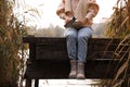 Woman with thermos sitting on wooden pier among reeds, closeup