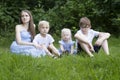 Woman with three children resting on grass in park. Young mother with daughter and sons sits on green lawn