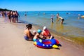 Woman and three children sitting on the beach next to an inflatable lifebuoy by the water