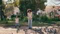 Woman throwing food pigeons standing in beautiful green park with cute daughter. Royalty Free Stock Photo