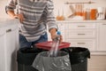 Woman throwing plastic bottle into trash bin in kitchen, closeup. Separate waste collection