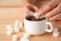 Woman throwing sugar into cup of tea on wooden table, closeup Royalty Free Stock Photo