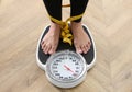 Woman tied with measuring tape using scale on floor, closeup. Overweight problem after New Year party