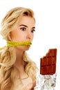 Woman with tied mouth holding bar of chocolate