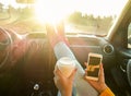 Woman toasting coffee take away go cup and using smart phone inside car with feet in warm socks on dashboard - Travel and trend Royalty Free Stock Photo