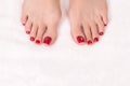 Woman toes with classic glossy red pedicure on white terry towel, close up. Female bare feet.