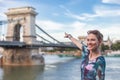 Woman with toothy smile pointing to Chain Bridge at Budapest, Hungary