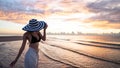 Woman in top bikini and white long pant wearing hat on the beach with a beautiful sunrise or sunset in background Royalty Free Stock Photo