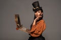 Woman in top hat with goggles using steampunk laptop isolated on grey