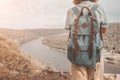 Woman with tourist backpack stands on top of a cliff and admires the panorama of a river or lake